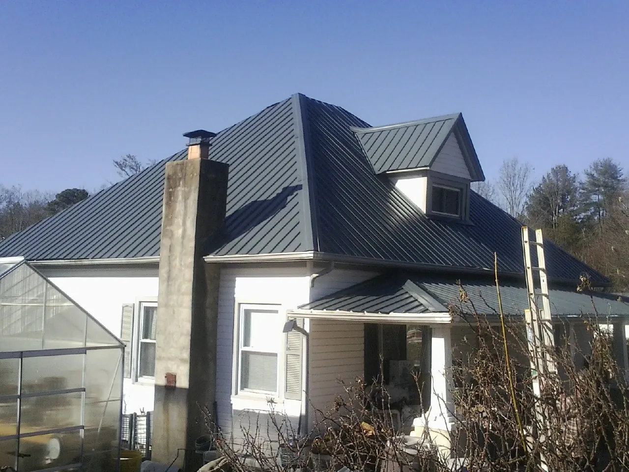 Dark blue standing seam metal roof on a white farmhouse with dormer — Slate & Tile Roof Repair by Roofing Brothers in Wimbledon