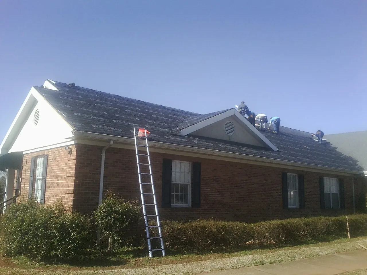 Crew tearing shingles off a brick ranch roof with a ladder set — Metal Roof Repair work by our crew in Wimbledon