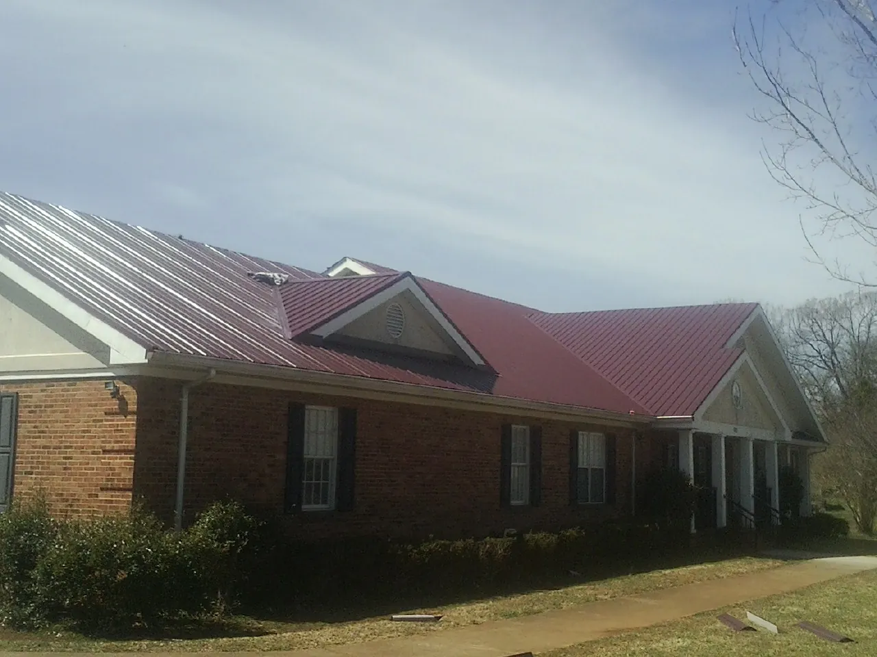 Red metal roof with gabled entries on a long brick building, from a Hail Damage Roof Repair job in Wimbledon