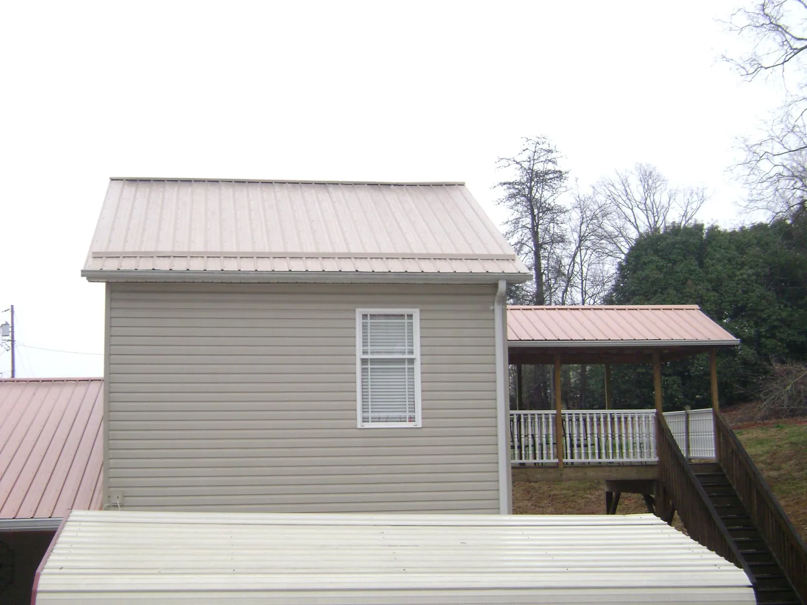 Tan metal roofs on a two story addition and attached porch, from a Roof Replacement job in Wimbledon